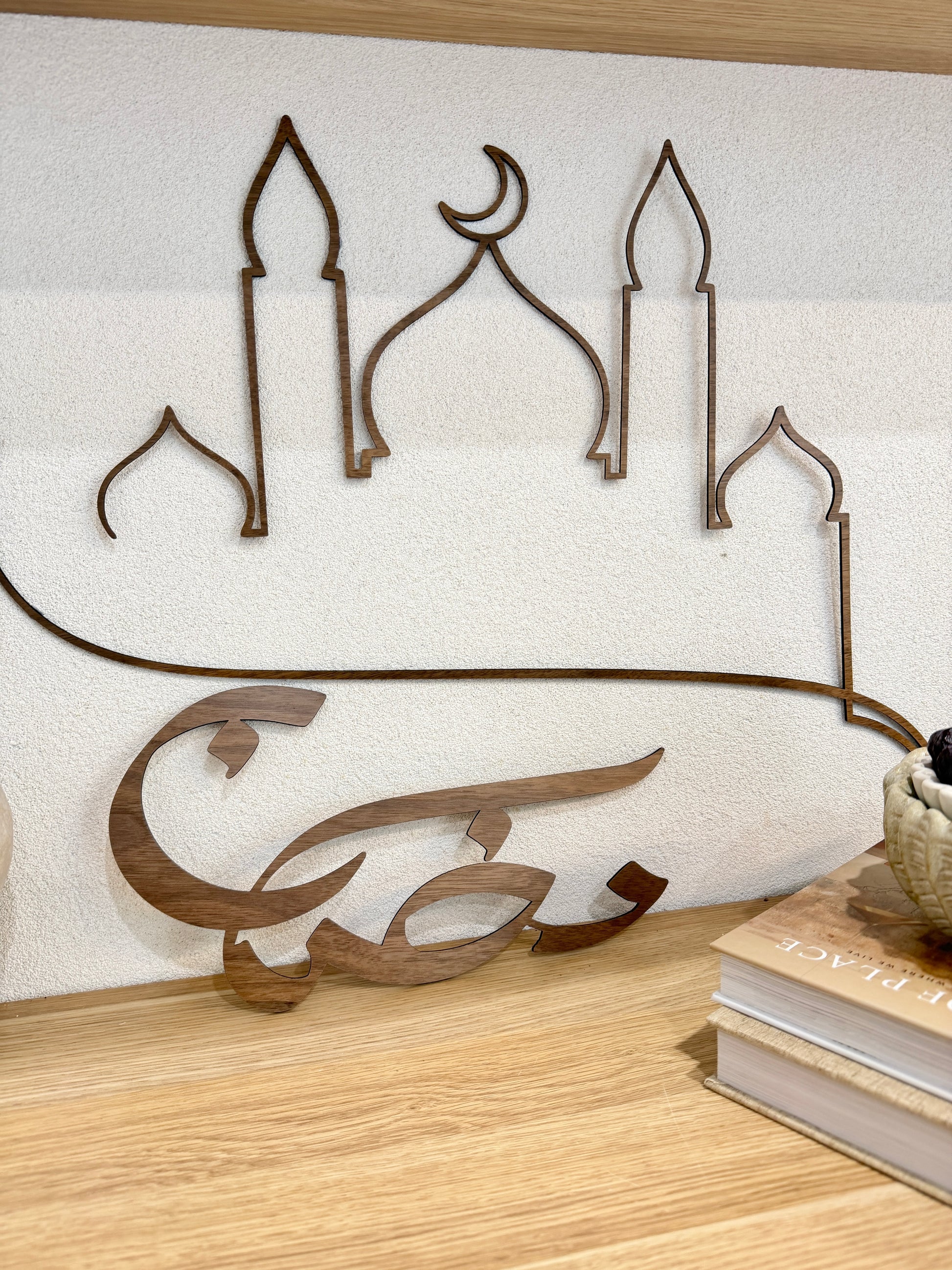 Decorative metal wall art with Arabic calligraphy on a white wall.
